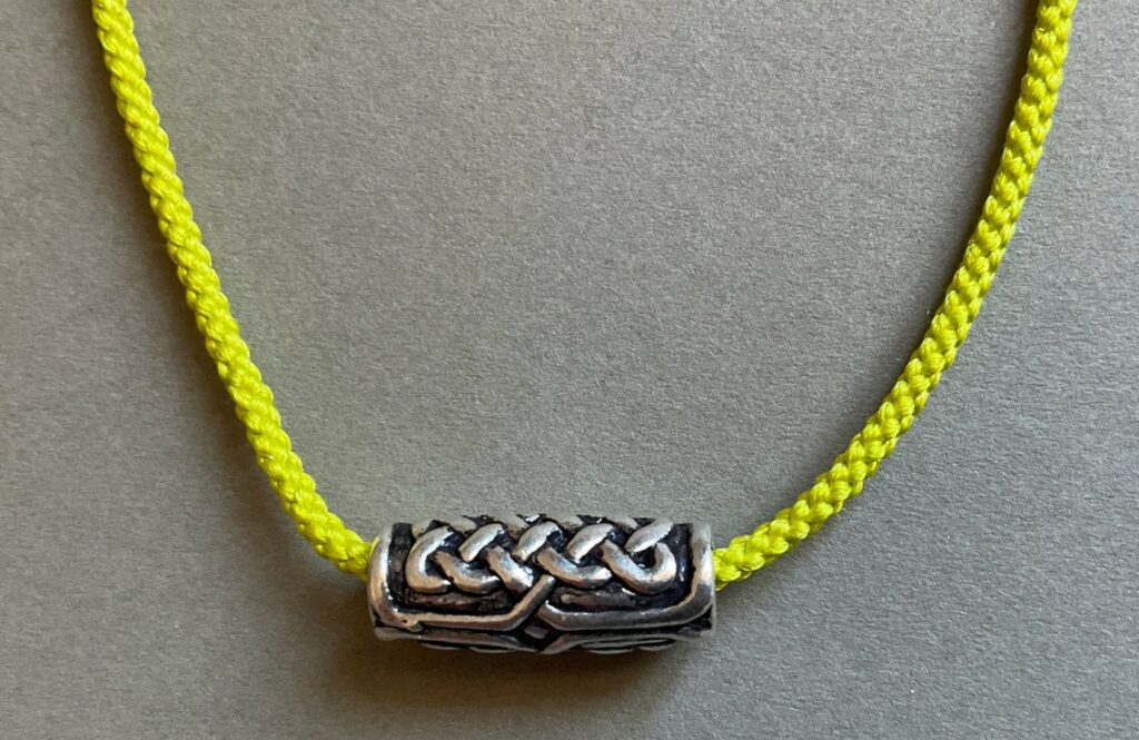 Yellow braided thread with metal bead on grey background.