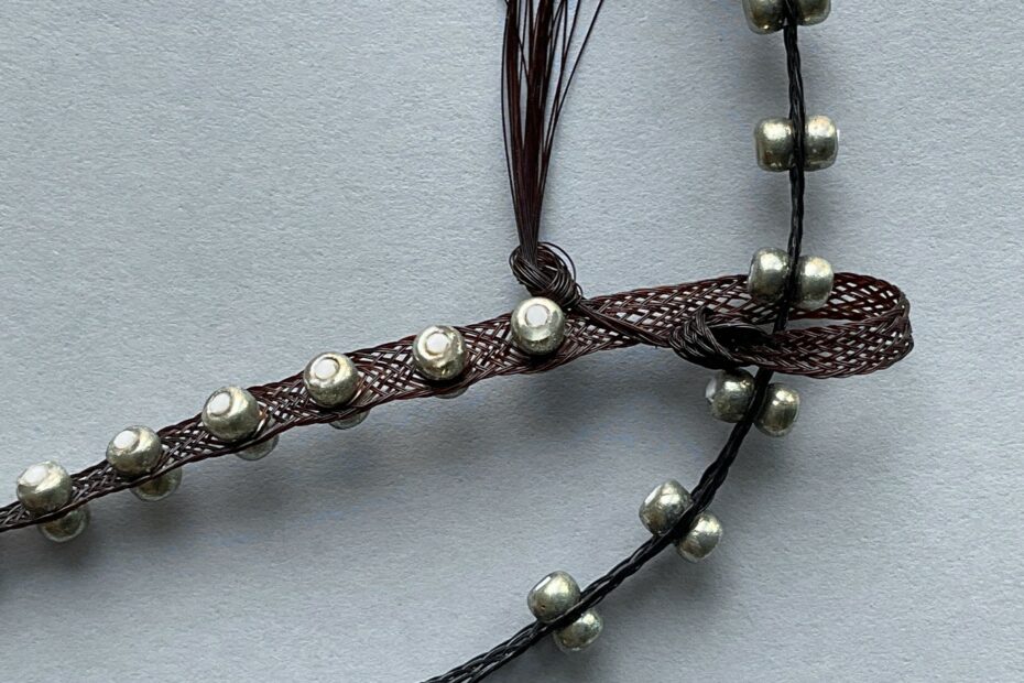 Reconstructed braid made of black thread with silver studs on grey background.